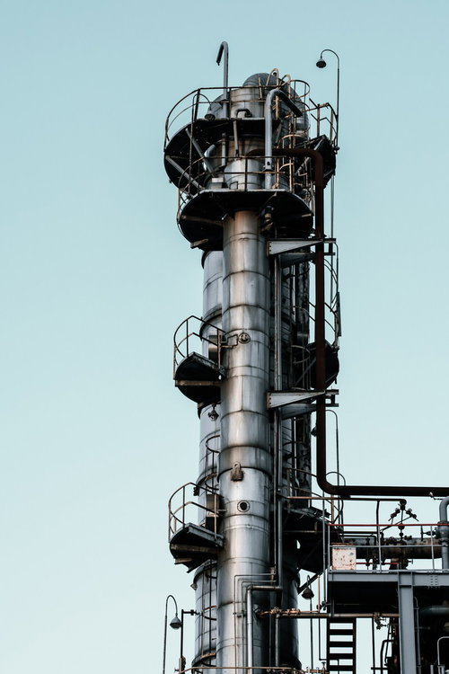 晴れた空に金属の円柱に階段やパイプが何段も取り付けられた工場の煙突