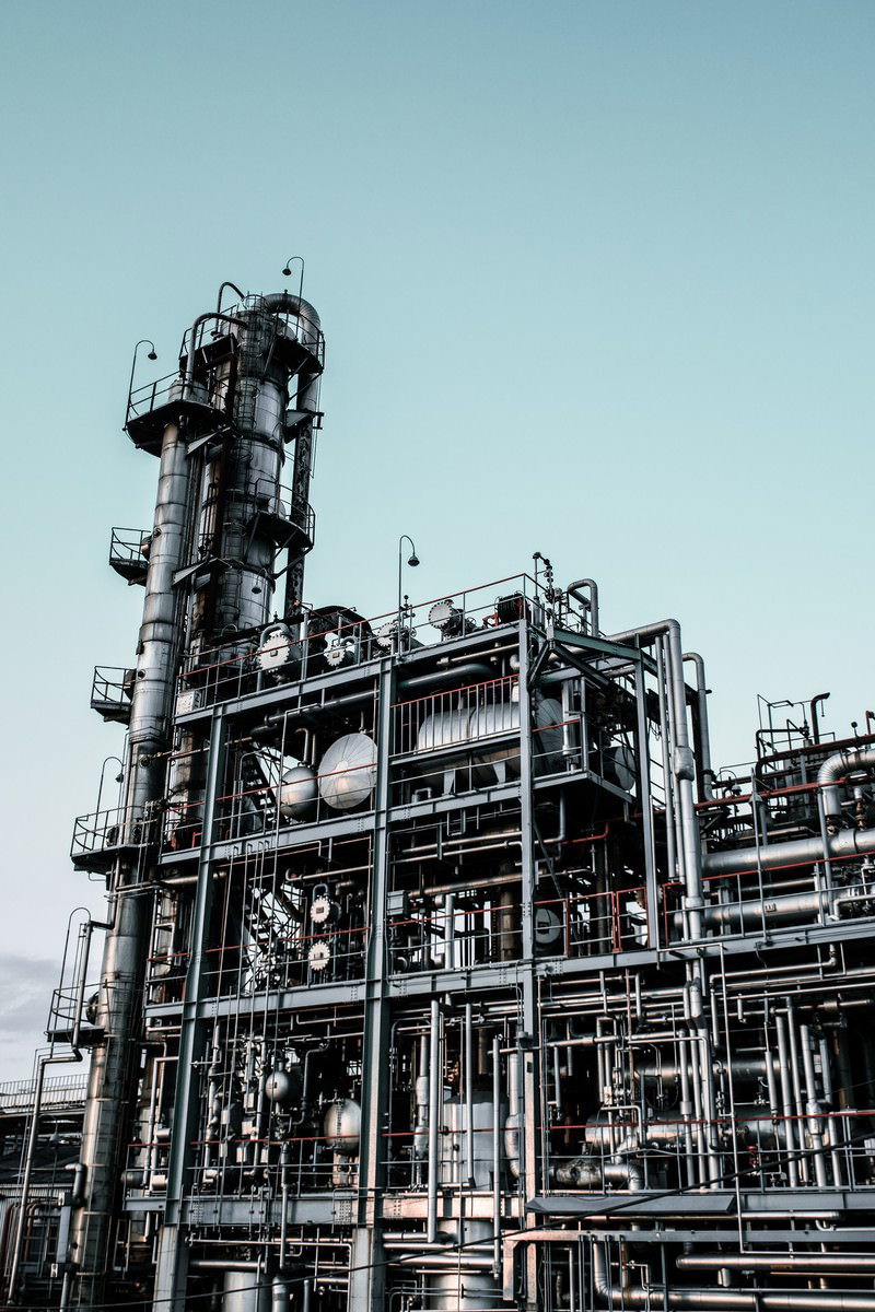 晴れた青空の下に配管やタンクや階段が複雑に組み合わさった工場設備