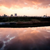 川の水面に映る夕焼け空と向こう岸の建物と草の土手の写真
