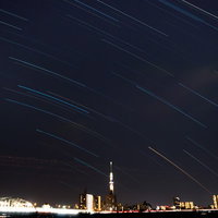 夜空に斜めの光の筋と照明で照らされたスカイツリーの都市夜景の写真