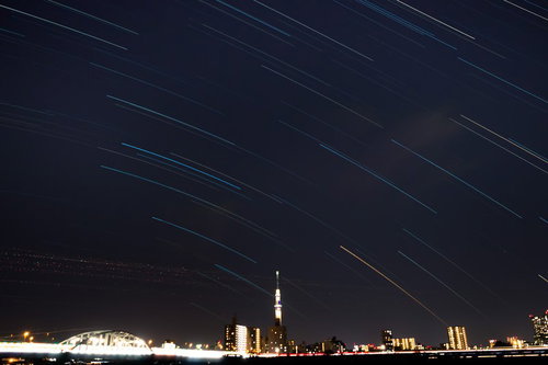 夜空に斜めの光の筋と照明で照らされたスカイツリーの都市夜景