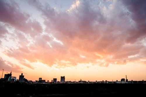 雲が広がる夕方の空と地平線に黒いシルエットで並ぶ都市の建物群
