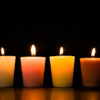 灯りをともしたキャンドルの並び、クリーム色からダークオレンジまで4色の写真