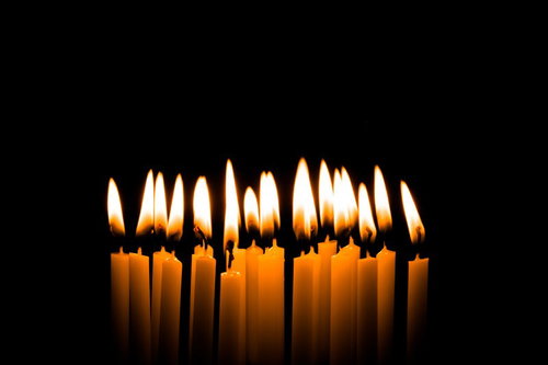 火がついた複数の和ろうそくが黒い背景に並ぶ