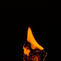 黒背景に揺らめく炎が燃えて灰になりかけの焚き火の写真