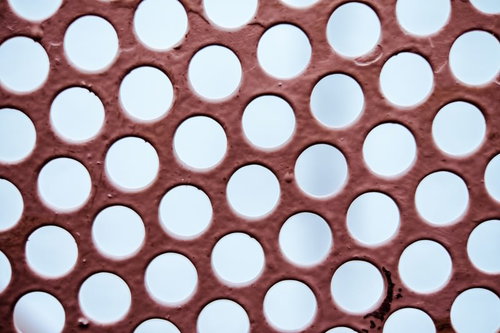 赤茶色の穴あき板に規則正しく並ぶ丸い穴のテクスチャー