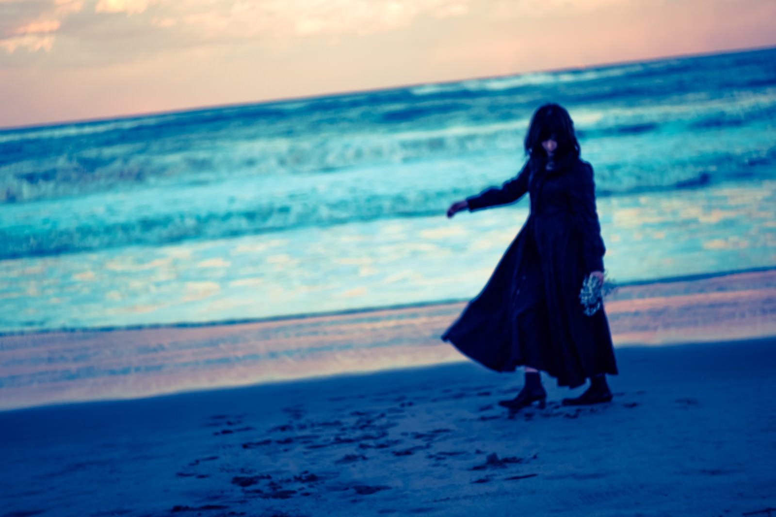 夕暮れの浜辺に立つ黒服の女性シルエット