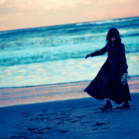 夕暮れの浜辺を彷徨う黒服の女性のシルエットの写真