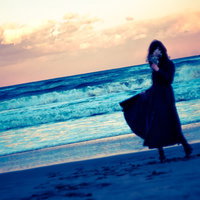 思い出に花を手向ける、夕暮れの波打ち際を歩く女性の写真