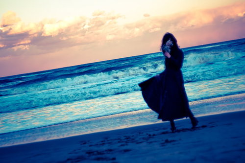 思い出に花を手向ける、夕暮れの波打ち際を歩く女性