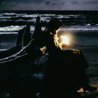 夜の海岸で流木の隙間から漏れる灯りの写真