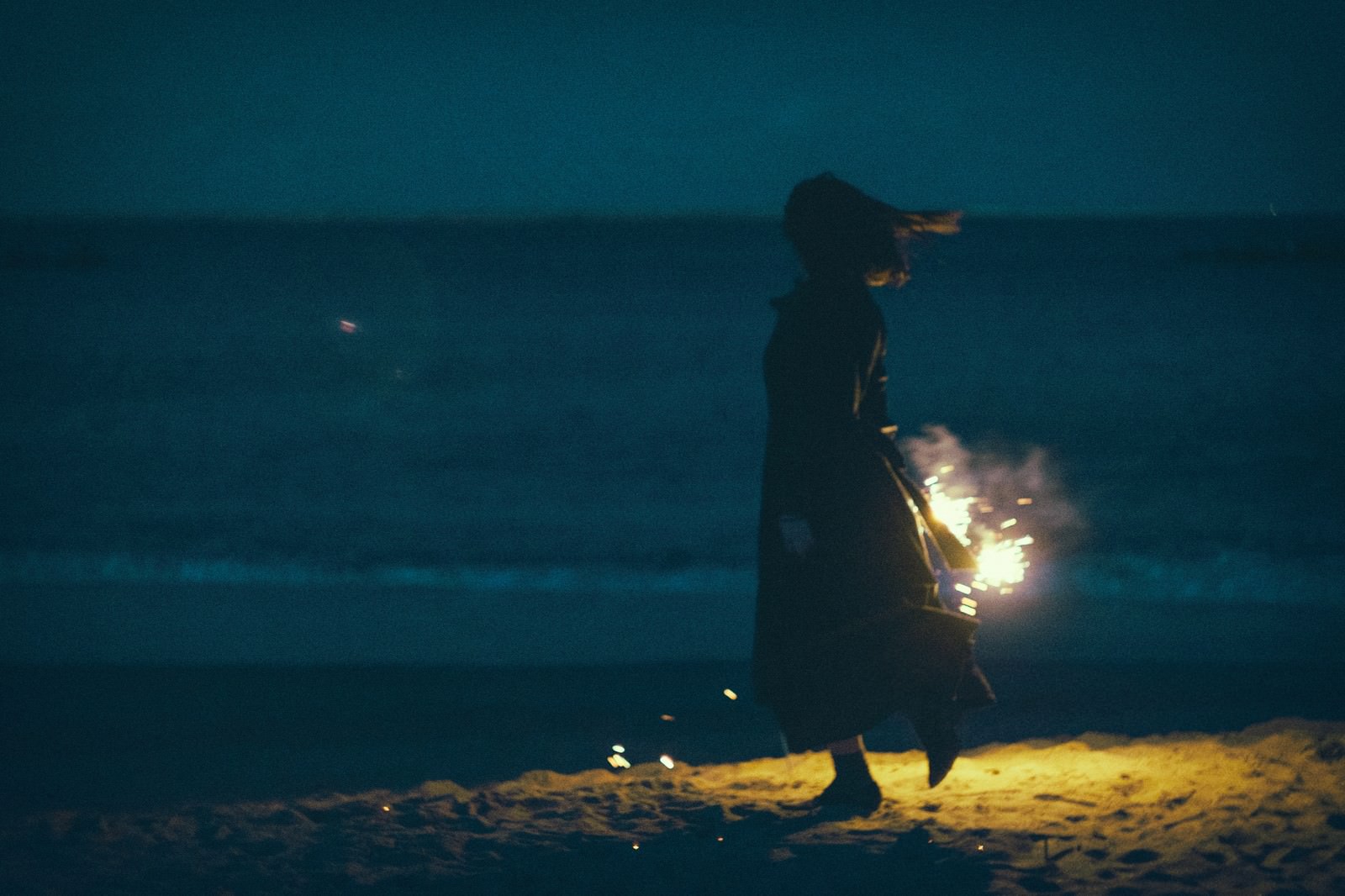夜の海岸で手持ち花火をする女性のシルエット