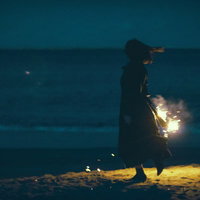 夜の浜辺で手持ち花火を持つ女性のシルエットの写真