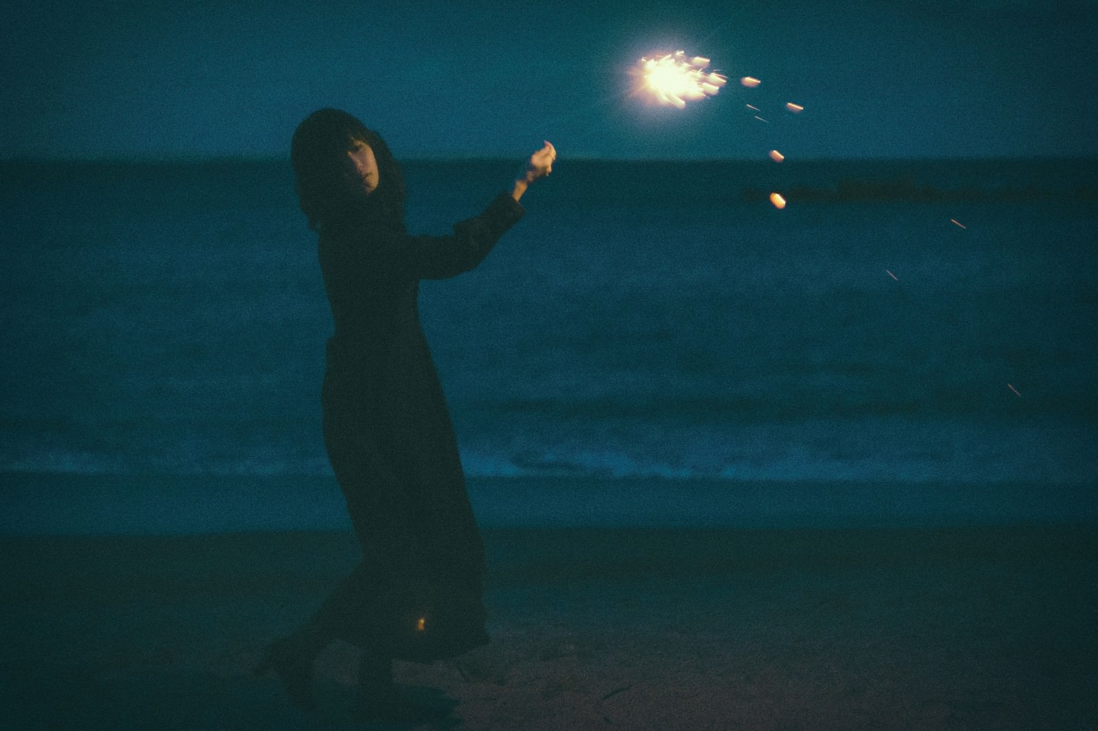 夜の砂浜で手持ち花火をする女性のシルエット