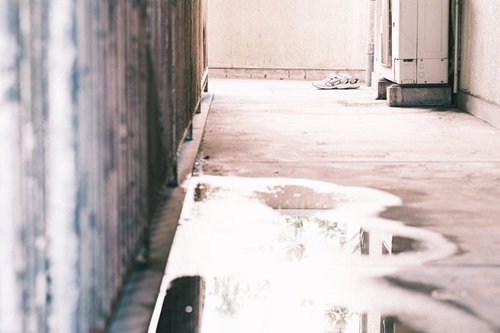 雨上がりの廊下に放置されたスニーカーと水溜り