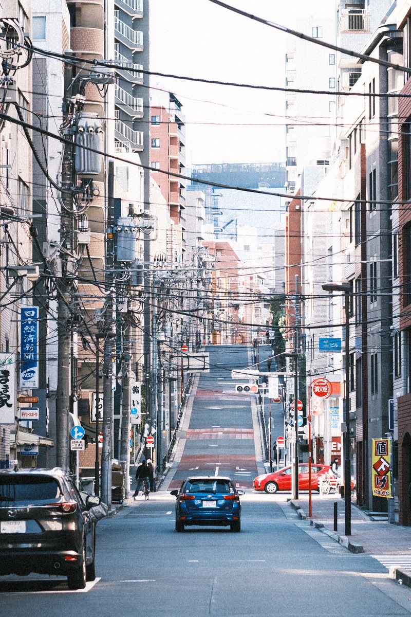 電線が複数張り巡らされた都市の車道と街並み