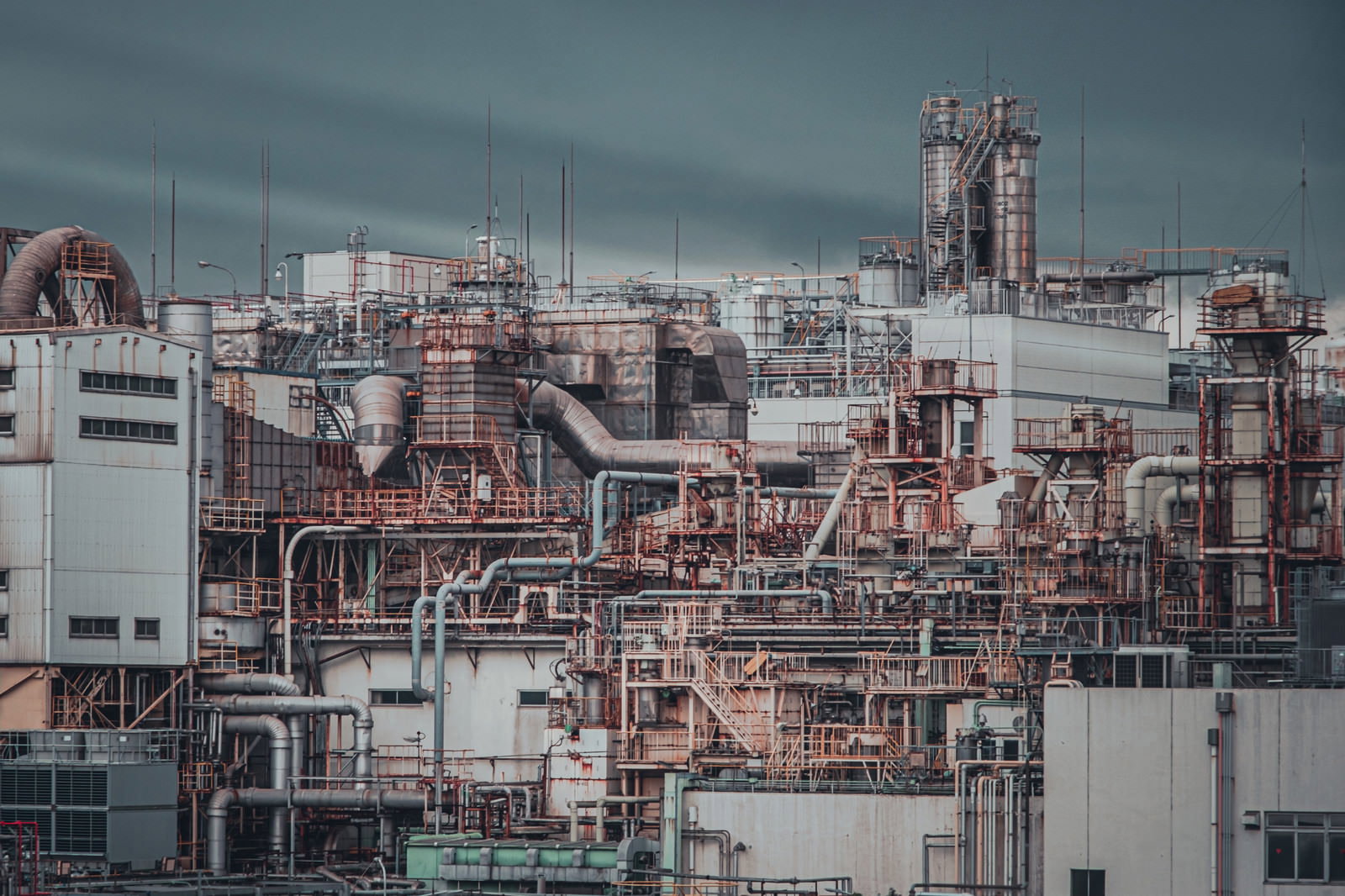 曇り空の下に立ち並ぶ工場のプラント設備と配管システム