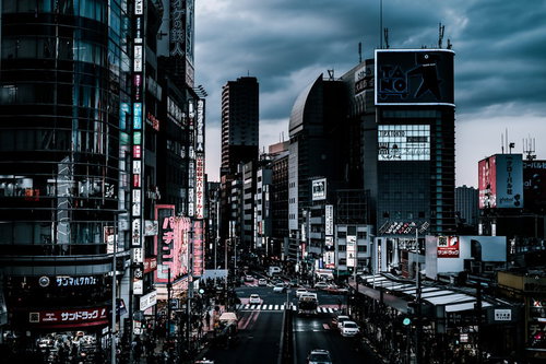 夕暮れ過ぎの新宿大ガード西の交差点前、ネオンが灯る繁華街