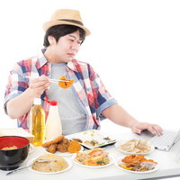 コロッケを食べながらコロッケレシピをパソコンで検索する男性の写真