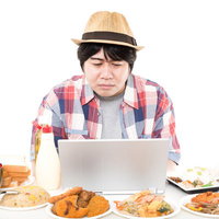 周りにある揚げ物や炭水化物が気になって仕事が手に付かないインテリ肥満男性の写真