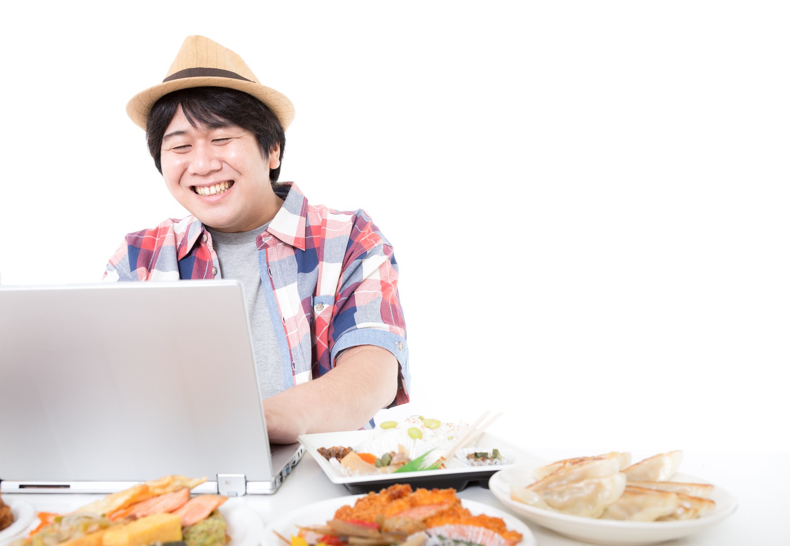 ノートパソコンを見ながら揚げ物を食べるチェック柄シャツの男性。テーブルに複数の食事容器。［モデル：あまのじゃく］