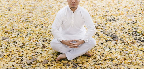 落ち葉に囲まれた修行中の男性が瞑想する姿