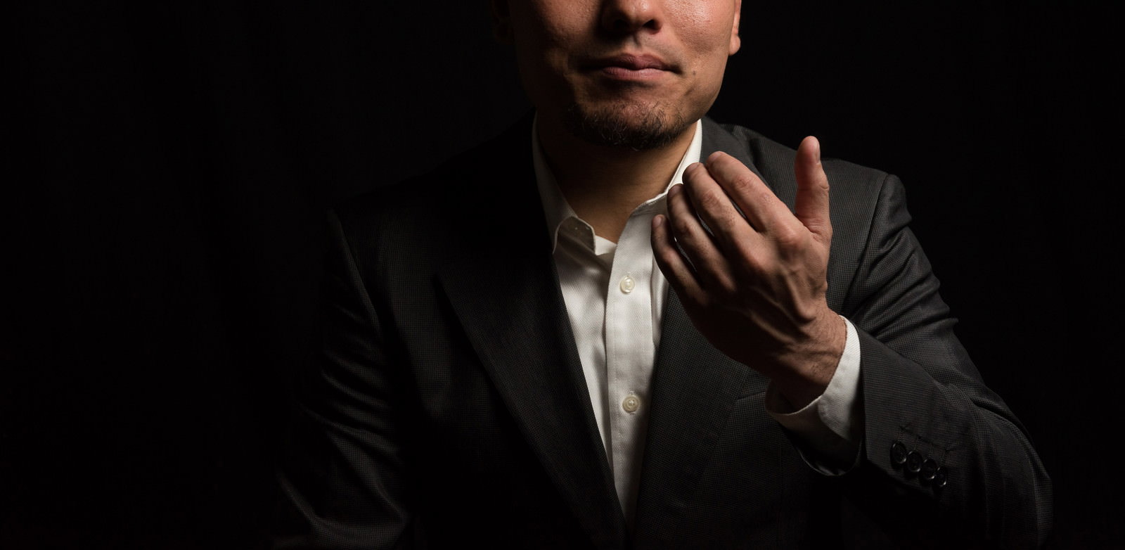 暗い背景の中でスーツを着た男性が手を差し伸べているポーズ