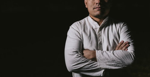 暗闇の中で腕を組み凝視する白いシャツの男性が深い思考に耽る