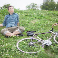 草原で自転車の目的地についてくつろぐ自転車男子の写真