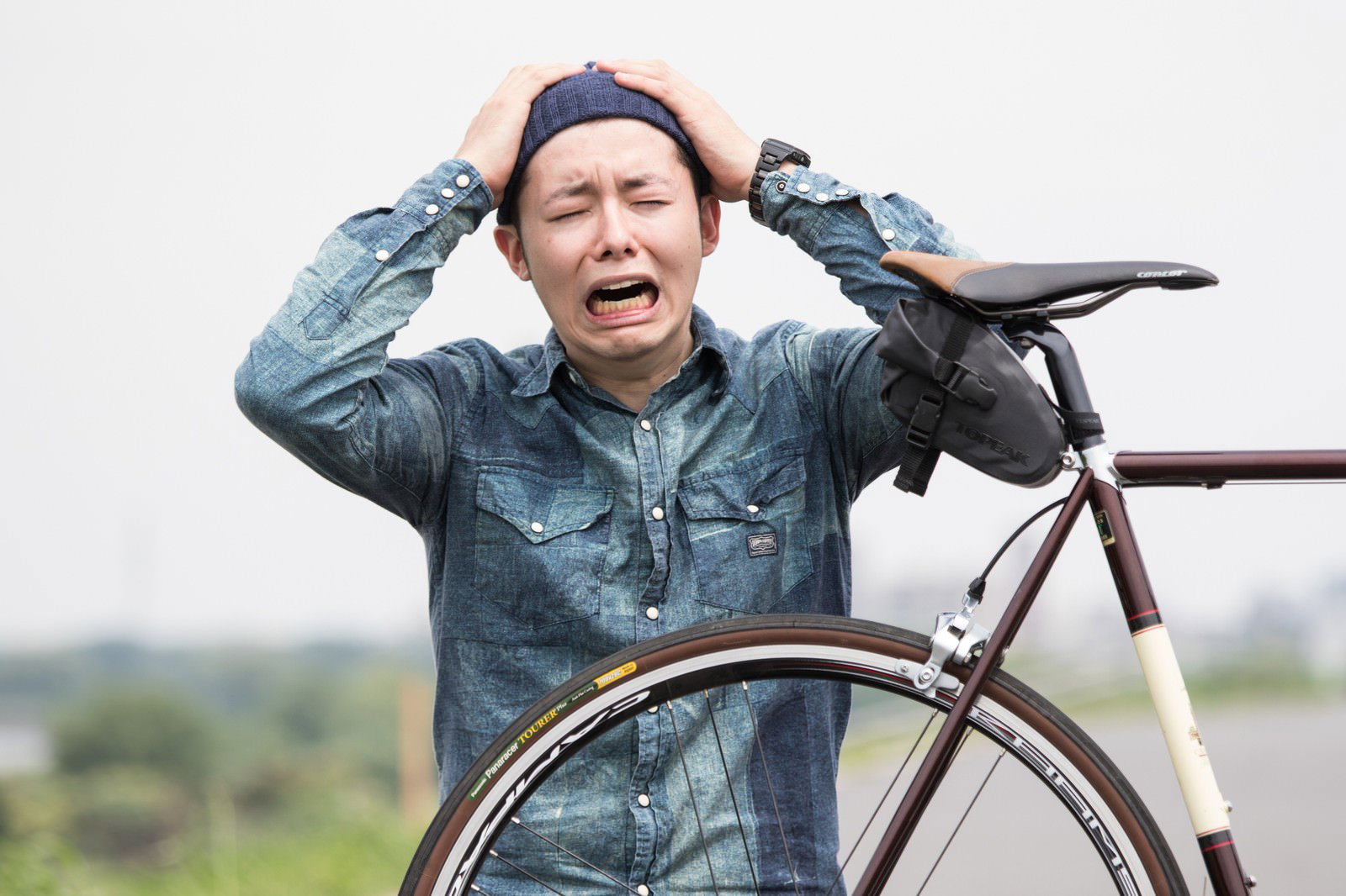 自転車のパンクに頭を抱えて叫ぶデニムシャツの男性［モデル：けんたさん］