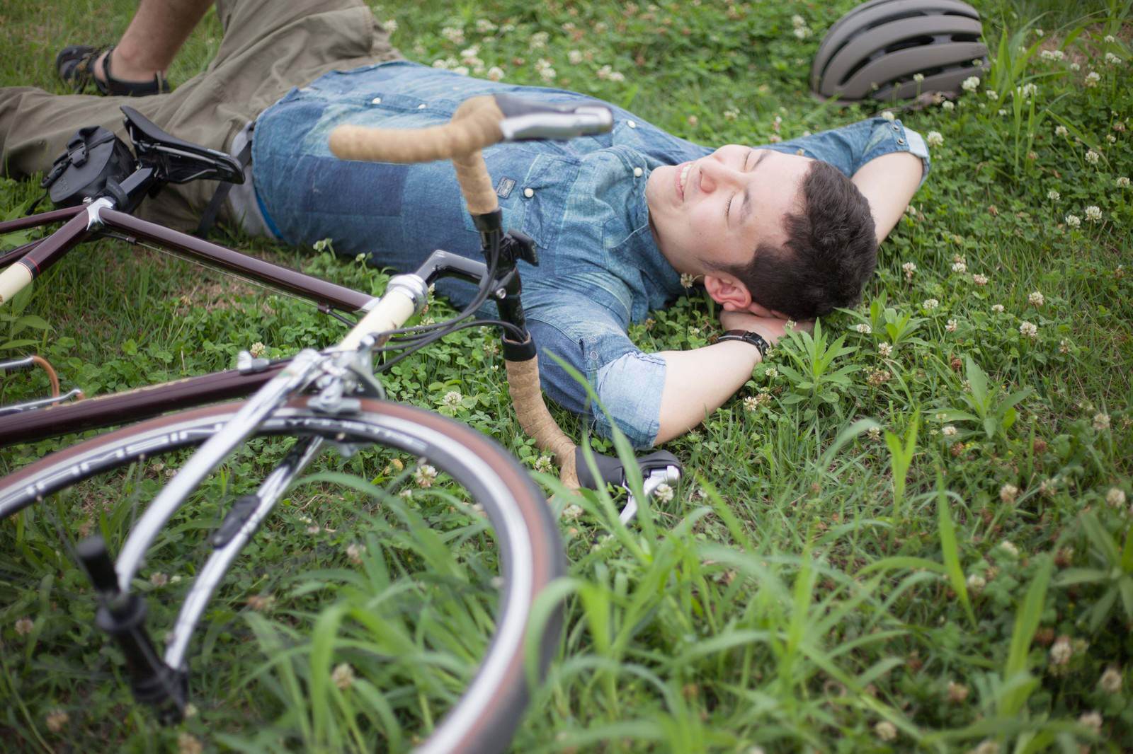 草地に仰向けで寝転ぶ自転車男性［モデル：けんたさん］