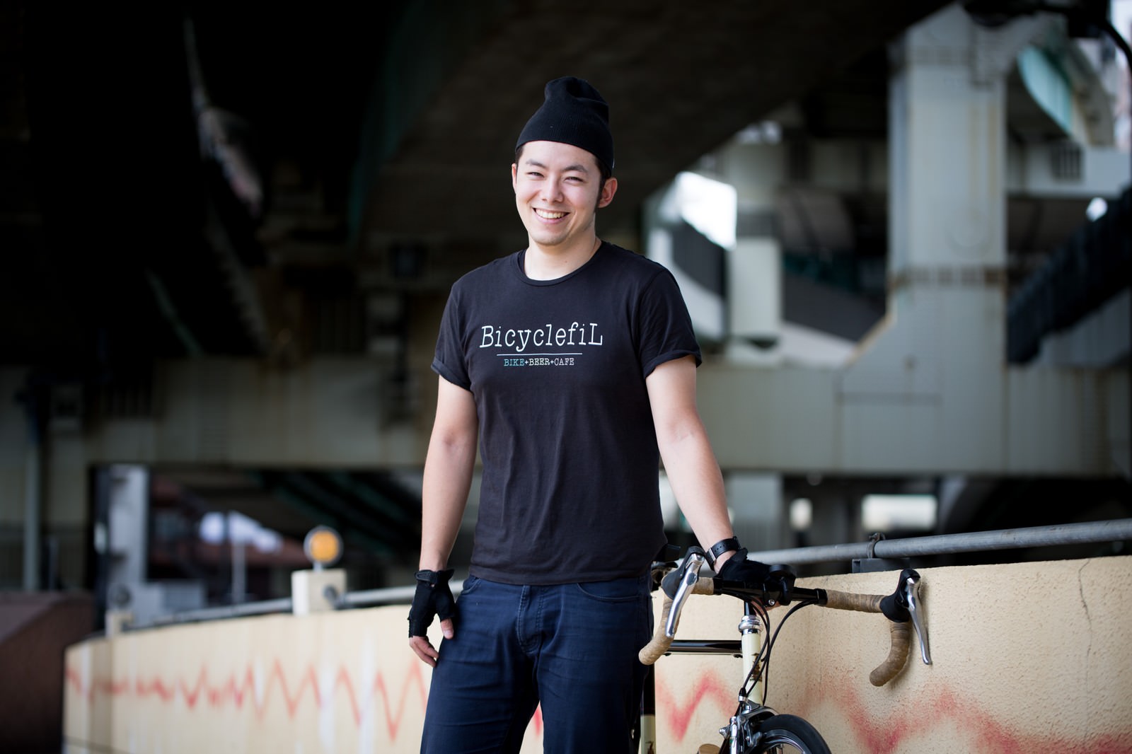 高架下でロードバイクを持ち笑顔の男性［モデル：けんたさん］