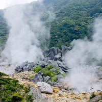 緑の山に囲まれた噴気孔から蒸気をあげる大涌谷の写真