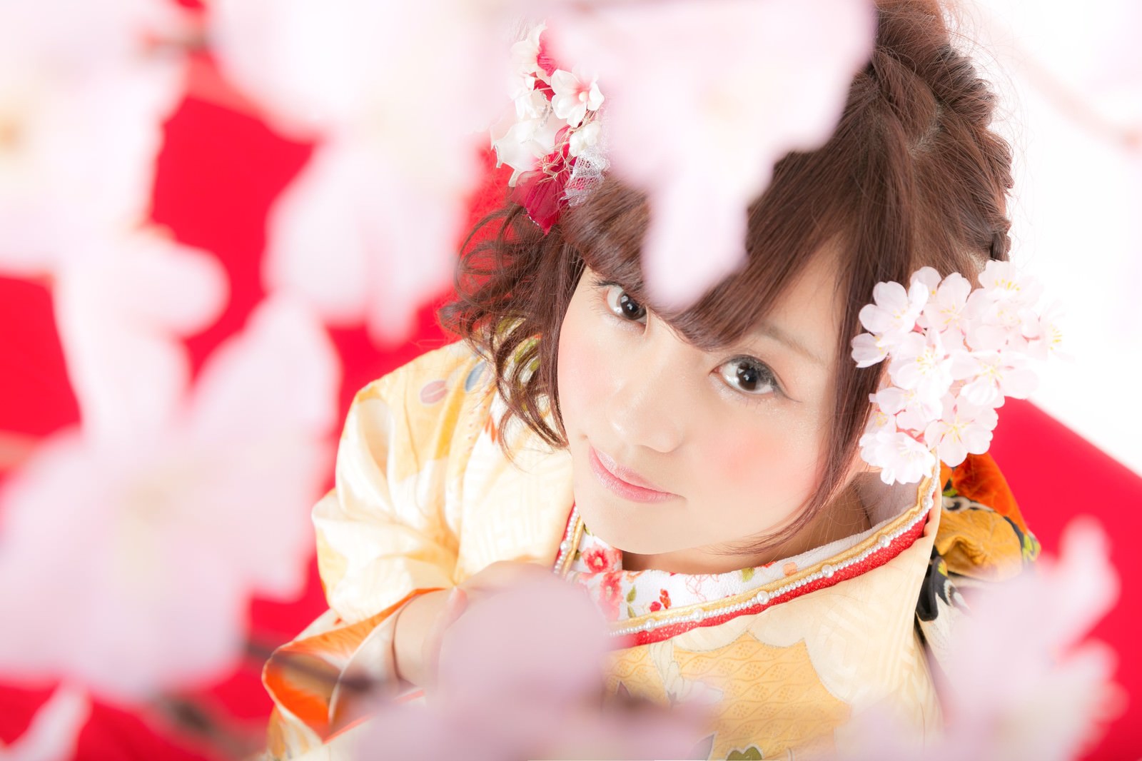 黄色い着物に花飾りをした女性が桜に囲まれてほほ笑む［モデル：河村友歌］