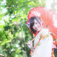 境内で赤い和傘をさす着物姿の新成人女性の写真