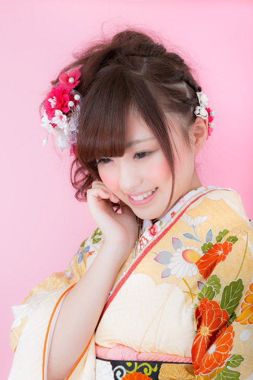 ピンクの髪飾りを付けた振袖姿の若い女性が微笑むの写真