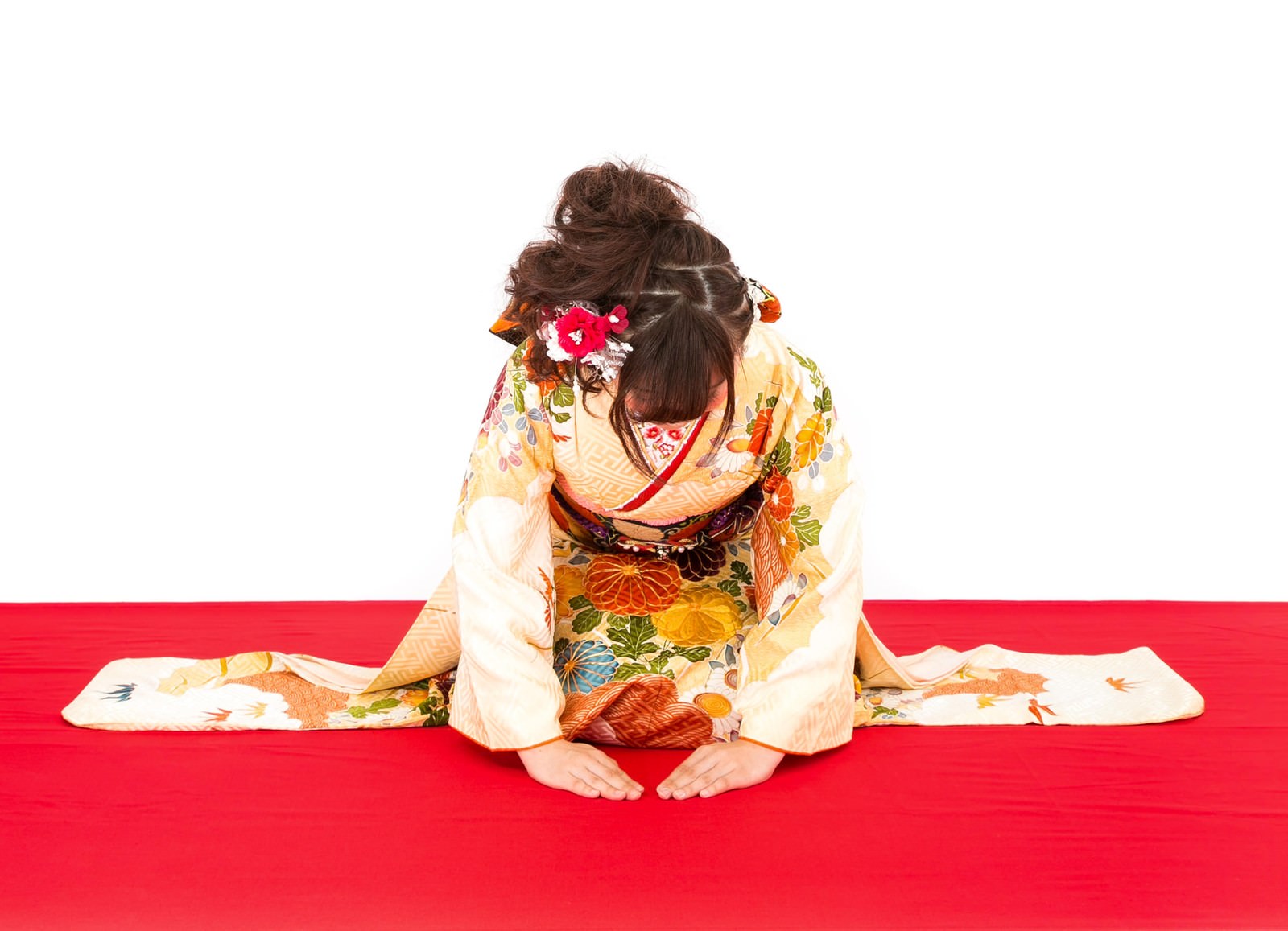 赤い正月飾りの前で着物姿で挨拶する女性［モデル：河村友歌］