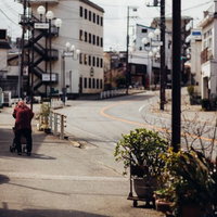 閑散とした地方の街を歩く赤い服の老婆の後ろ姿の写真
