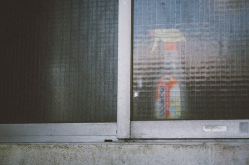 老朽化したアパートの窓に置かれた洗剤ボトル