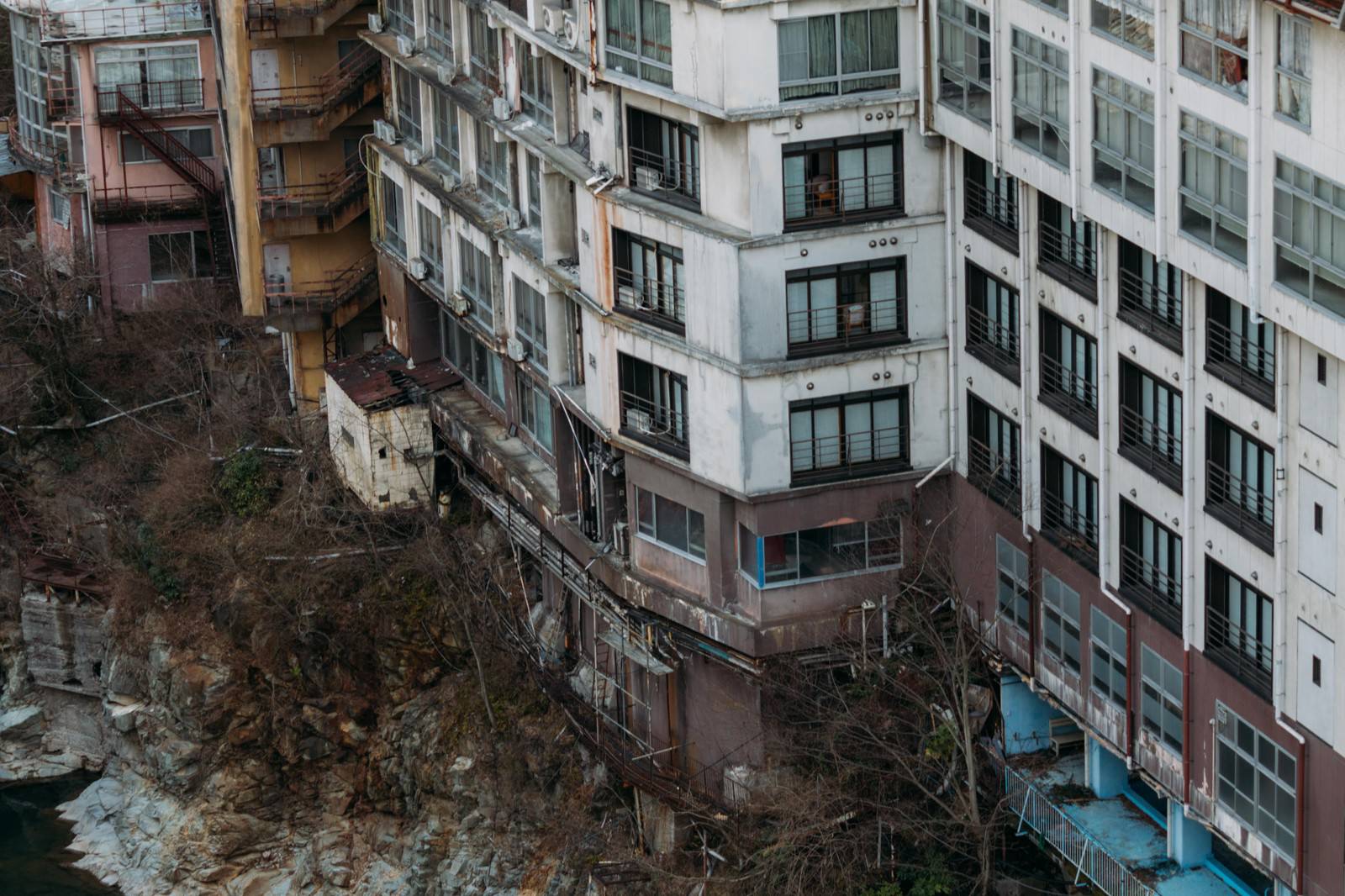 鬼怒川沿いに建つ老朽化した廃墟ホテル、白い壁が剥落し窓が黒い複数の建物