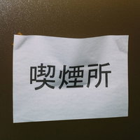 茶色のざらざらした壁に貼られたA4コピー用紙の喫煙所表示の写真
