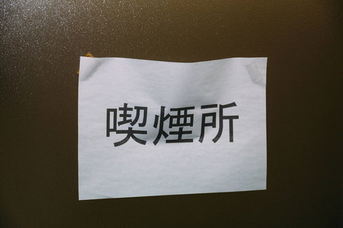 茶色のざらざらした壁に貼られたA4コピー用紙の喫煙所表示