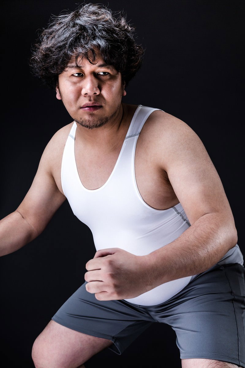 白いタンクトップを着た男性が黒い背景の前に腰をかがめている［モデル：あまのじゃく］