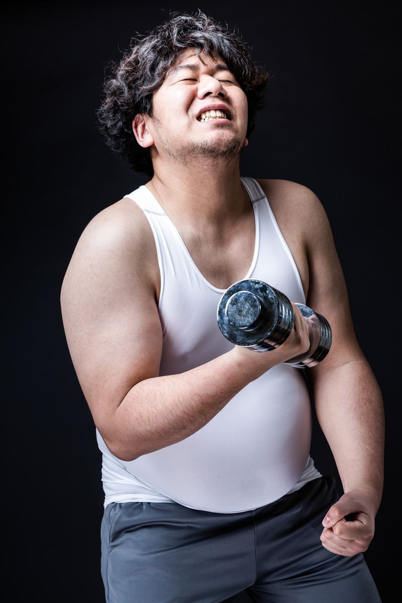 ダンベルを持ってトレーニングする笑顔の男性［モデル：あまのじゃく］