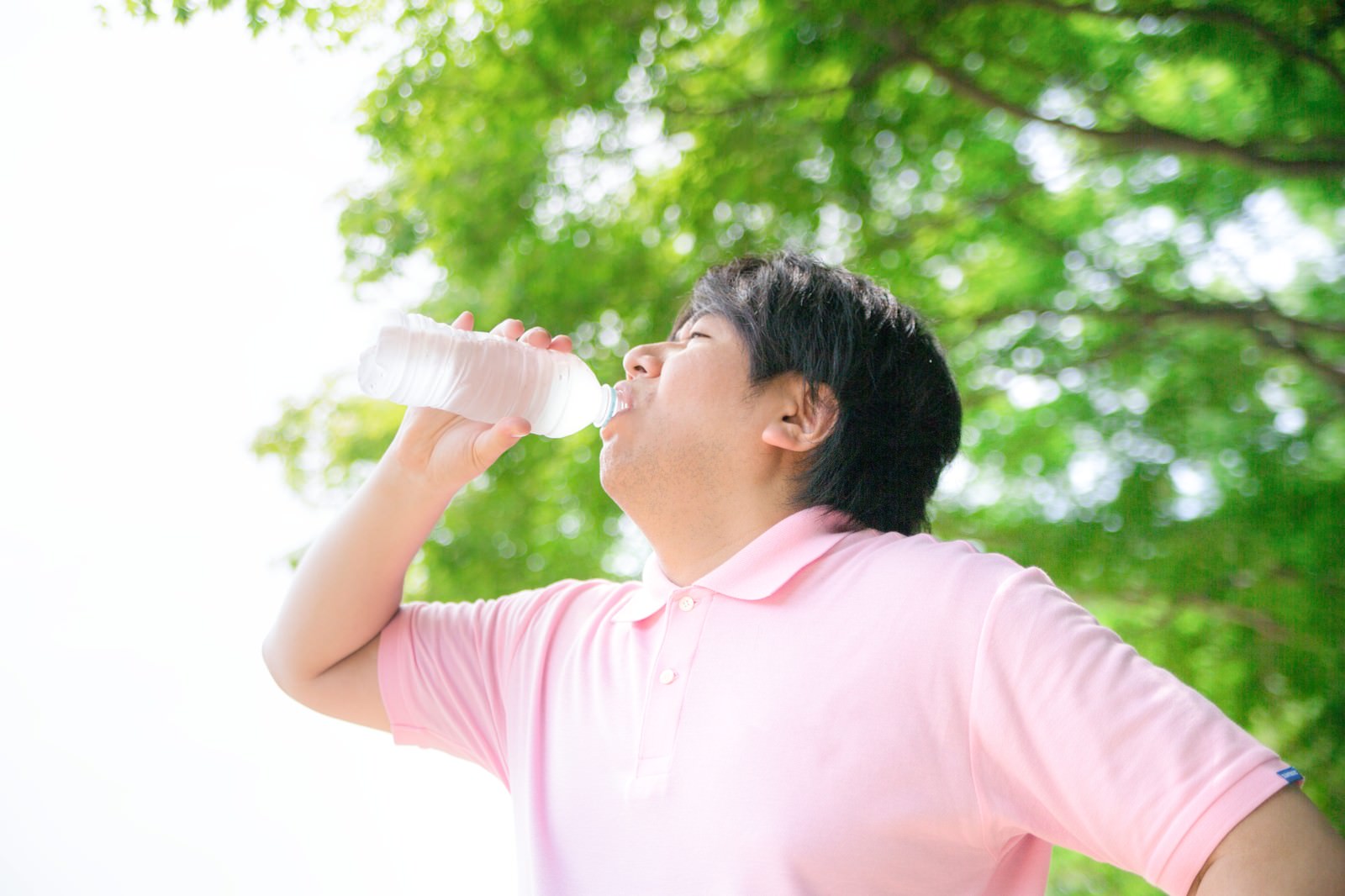 ペットボトルから水をがぶ飲みする、ピンク色のポロシャツ姿の男性［モデル：あまのじゃく］