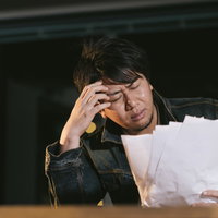 デスクで出来上がった原稿を見て頭を抱える男性ライターの写真