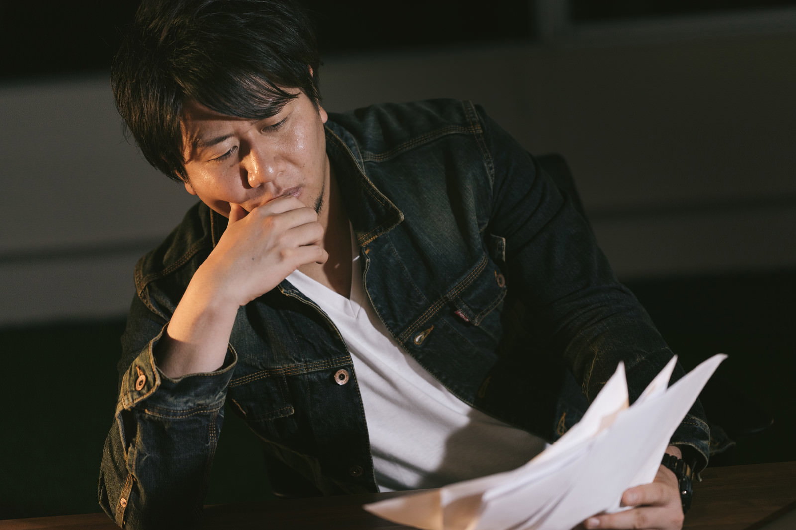 深夜に原稿を手に考え込む男性［モデル：あまのじゃく］