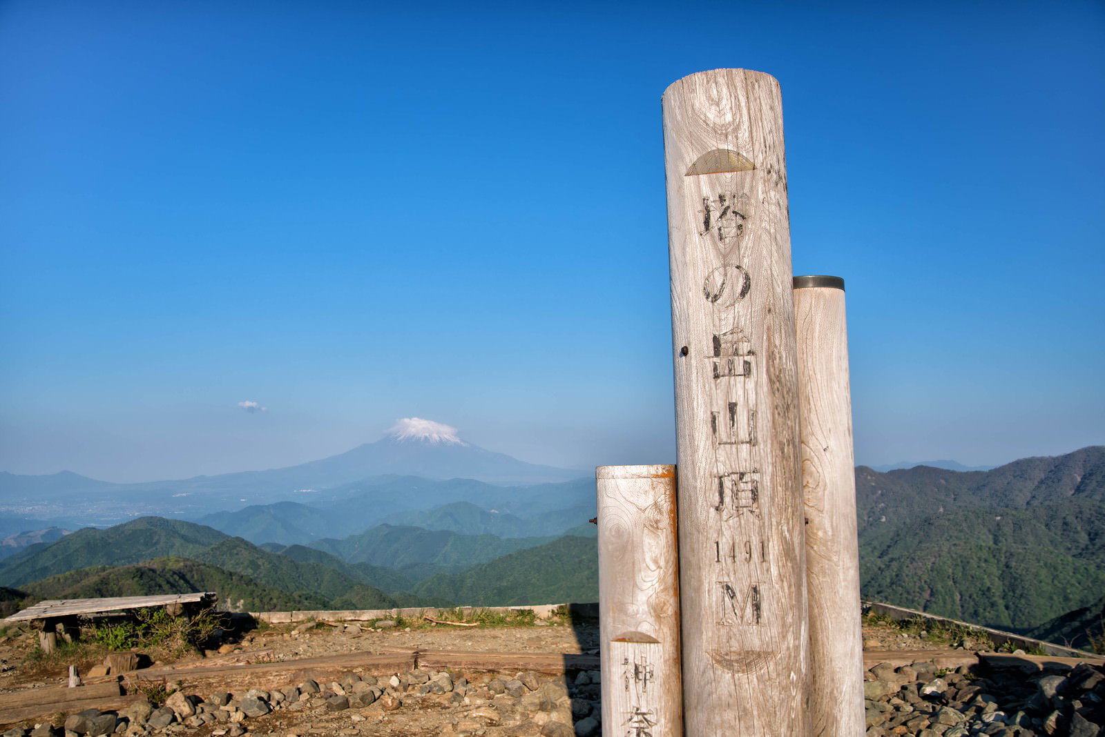 青空の下、塔ノ岳山頂に立つ木製標識と背景の山並み