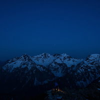 夜明け前の穂高連峰、深い青の夜空に浮かぶ雪化粧の連峰の写真