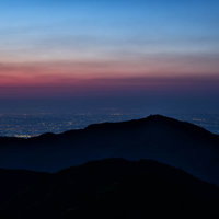 大山のシルエットと眼下に広がる街の夜景、夕焼けのグラデーションの写真